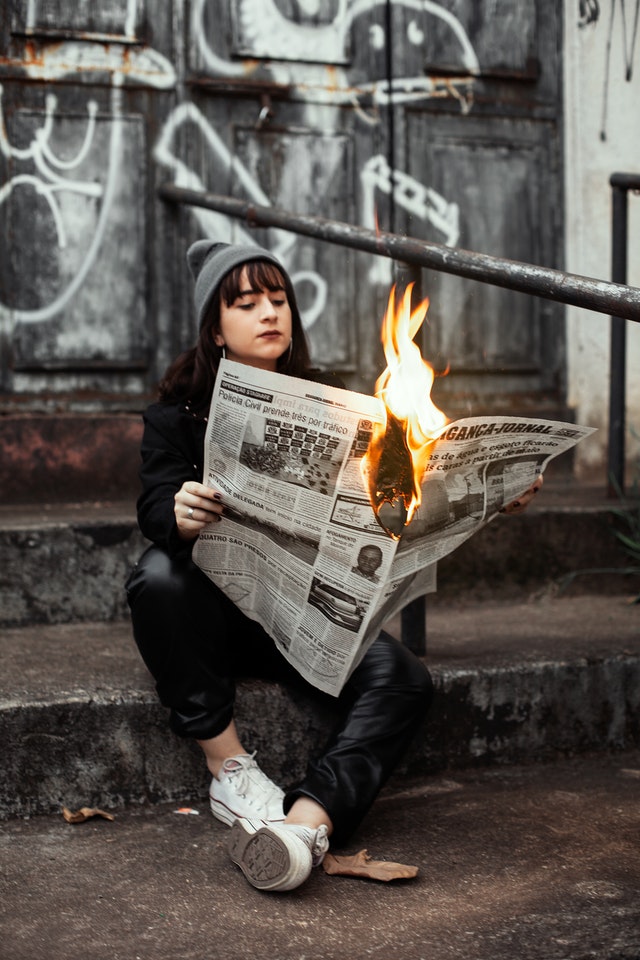 Adolescente leyendo periódico en llamas como simbolismo del agotamiento emocional que produce el continuo bombardeo de noticias negativas